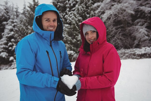 Portrait De Couple Souriant Dans Des Vêtements Chauds Tenant Coeur Enneigé