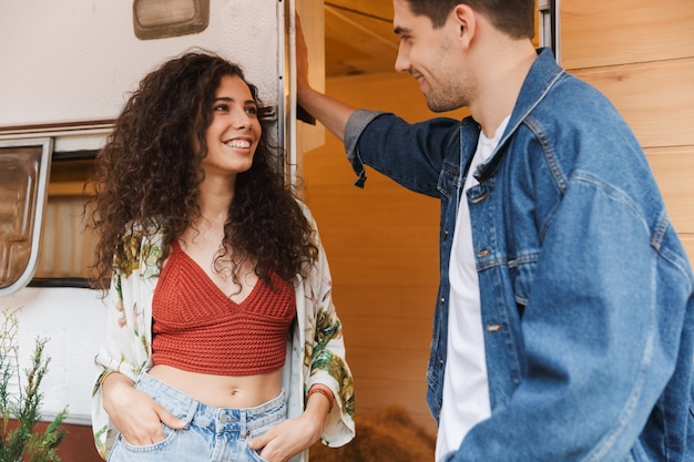 Portrait d'un couple souriant, homme et femme parlant ensemble tout en se tenant près de la maison sur roues à l'extérieur