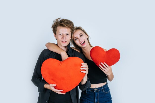 Portrait d'un couple tenant des coussins en forme de cœur sur les visages sur un fond blanc