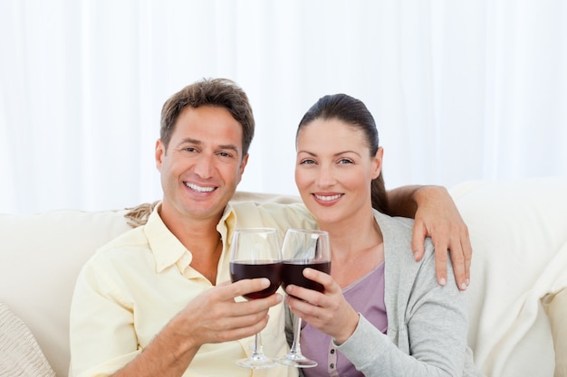 Portrait d&#39;un couple tinter les verres de vin rouge sur le canapé