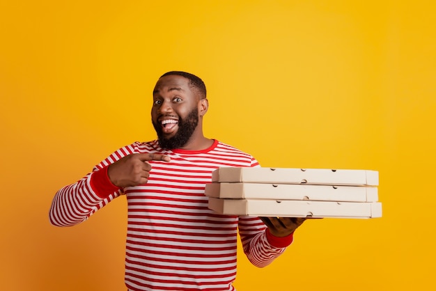 Portrait d'un coursier étudiant africain tenir des boîtes à pizza en pile pointer du doigt la promotion de la publicité