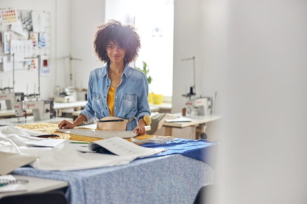 Photo portrait de couturière afro-américaine avec des outils debout à table de coupe