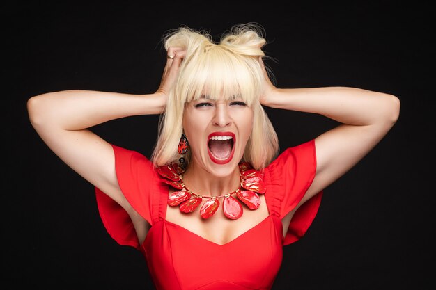 Portrait de crier femme blonde fashion en robe rouge tenant la tête ayant une émotion négative
