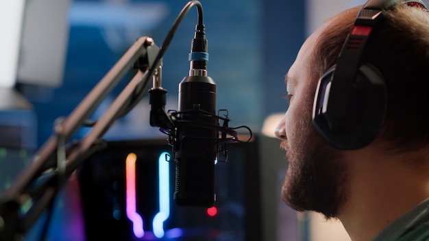 Portrait de cyber parlant en direct avec des joueurs utilisant un microphone et un ordinateur puissant. Homme streamer assis sur une chaise de jeu jouant à un jeu vidéo de tir spatial lors d'un tournoi d'esports en ligne.