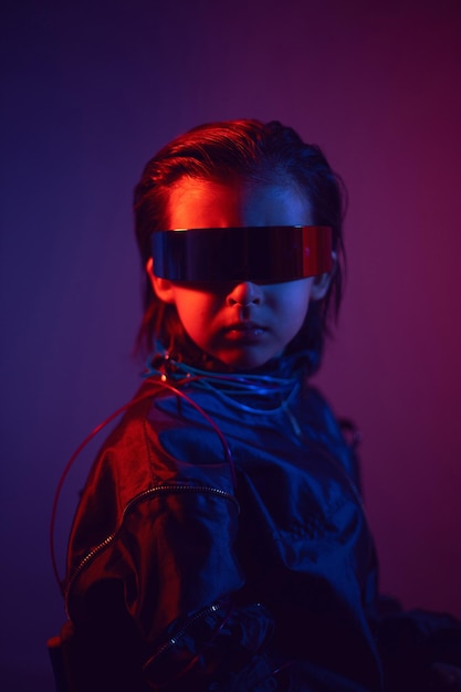 Portrait cyberpunk garçon enfant dans des lunettes vr dans des tons bleus et rouges avec des fils sur fond rouge