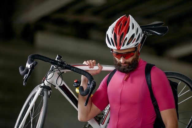 Portrait d'un cycliste debout sous un pont avec un vélo à la main posant devant la caméra sur un fond d'architecture Mode de vie actif Le cyclisme est un passe-temps