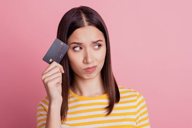 Portrait de dame confuse douteuse tenir la carte de débit côté espace vide prendre une décision d'investissement sur fond rose