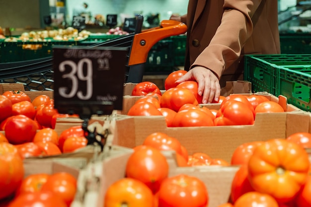 Portrait d'une dame du millénaire achetant de la nourriture marchant dans un supermarché avec un chariot Une cliente choisit des tomates en prenant des produits dans les étagères