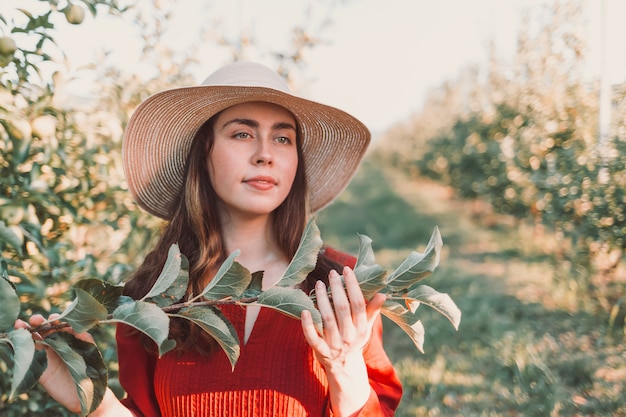 Portrait dans le jardin. Jeune et belle femme dans un chapeau et une robe rouge, avec une branche d'arbre dans ses mains