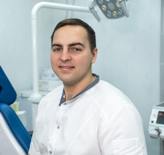 Portrait d'un dentiste professionnel souriant assis sur fond de cabinet dentaire