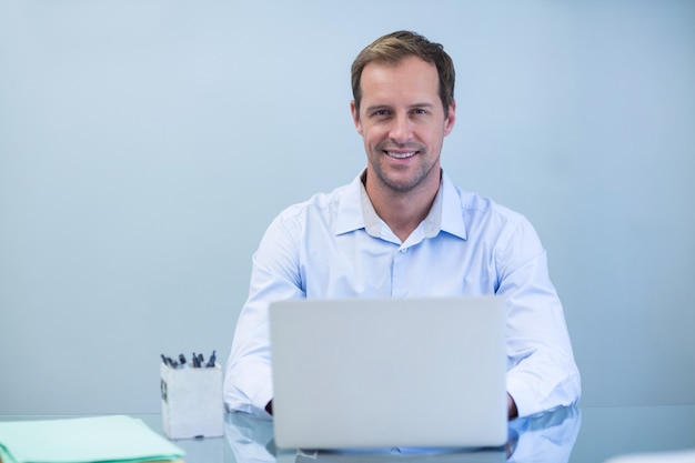 Portrait de dentiste souriant travaillant sur ordinateur portable