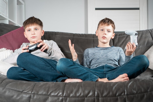 Portrait de deux adolescents bouleversés assis sur un canapé à la maison tenant un joystick de contrôleur de jeu jouant à des jeux vidéo