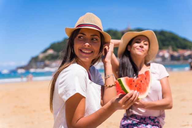 Portrait De Deux Amis En été Sur La Plage Mangeant Une Pastèque Avec La Mer En Arrière-plan Assis Sur Le Sable