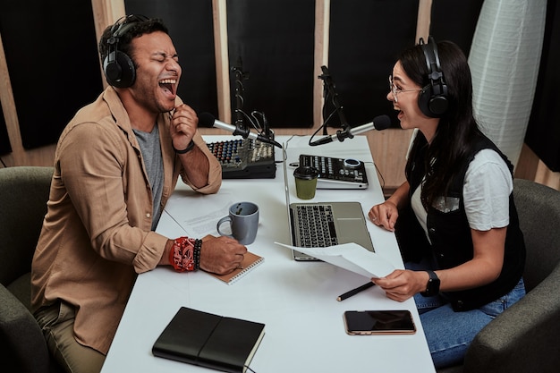 Portrait de deux animateurs de radio joyeux, jeune homme et femme riant tout en discutant de divers sujets