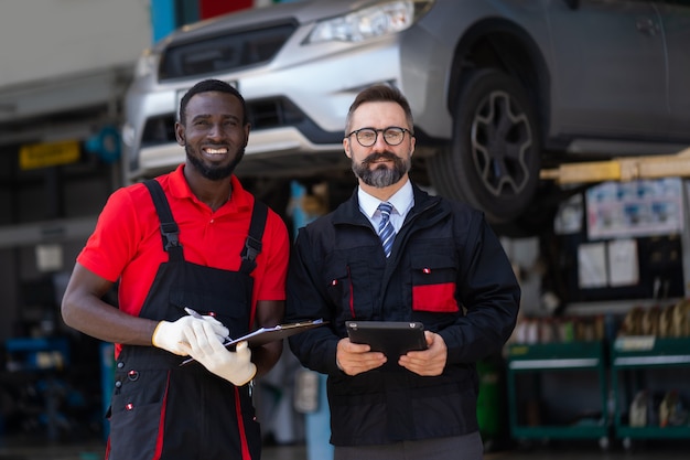 Portrait de deux beaux mécaniciens automobiles en uniforme debout ensemble au service automobile. La vie des Noirs compte. Hommes noirs et hommes blancs.