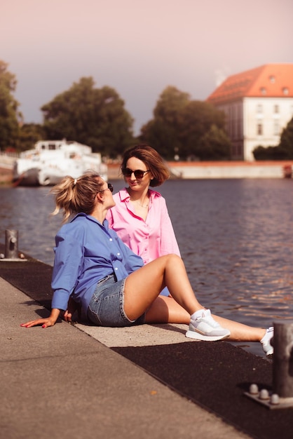 Portrait de deux belles jeunes femmes hipster souriantes dans des vêtements de couleur d'été à la mode femmes insouciantes posant sur fond de rivière Modèles positifs s'amusant étreindre