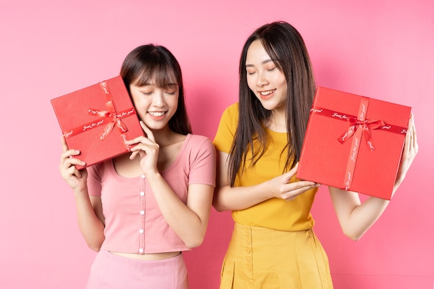 Portrait de deux belles jeunes filles asiatiques tenant une boîte-cadeau rouge sur un mur rose