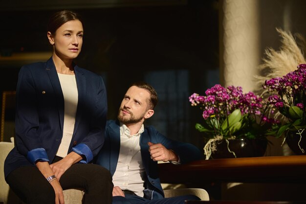 Portrait de deux belles personnes confiantes, collègues en voyage d'affaires, femme et homme de race blanche d'âge moyen, assis sur un fauteuil dans le salon d'un hôtel de luxe