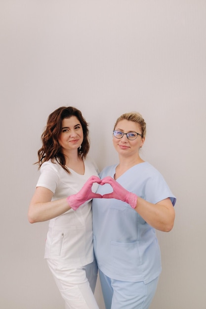 Portrait de deux cosmétologues qualifiées souriant en toute confiance et faisant un cœur avec leurs mains dans un centre médical