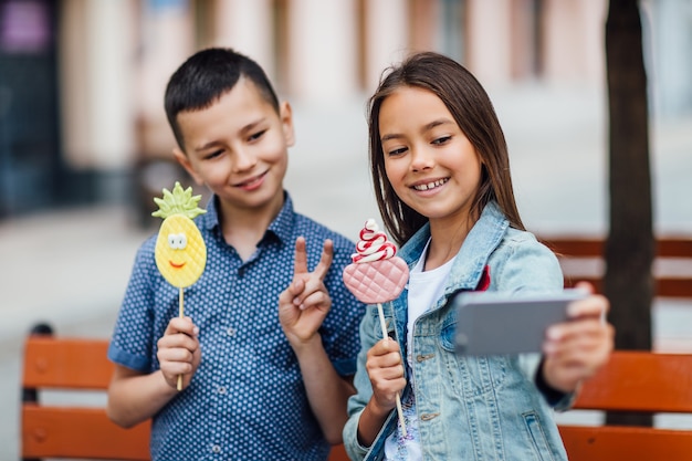 Portrait de deux enfants faisant un selfie un jour d'été avec des bonbons sur les mains et souriant.