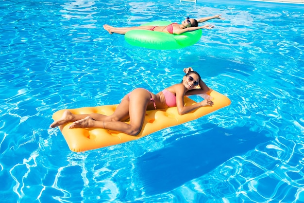 Portrait de deux femmes allongées sur un matelas pneumatique dans la piscine
