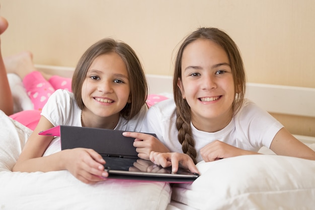 Portrait de deux filles souriantes au lit et à l'aide de tablette numérique