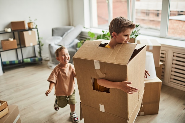 Portrait de deux frères portant des boîtes en carton et jouant pendant que la famille déménage dans une nouvelle maison copie s...