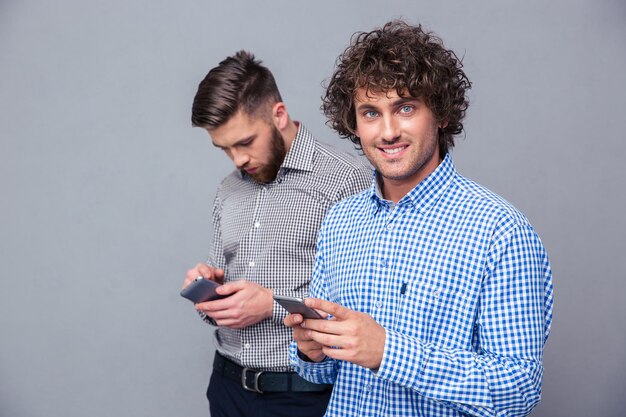 Portrait de deux hommes occasionnels à l'aide de smartphone sur mur gris