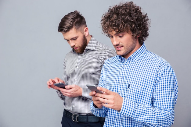 Portrait de deux hommes sérieux à l'aide de smartphone sur mur gris