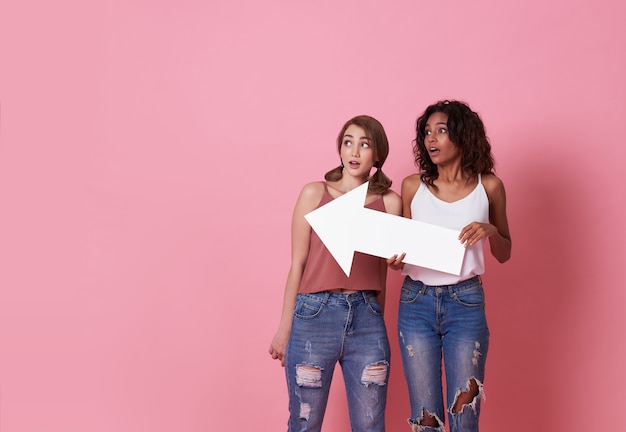 Portrait de deux jeune femme choquée debout avec sa flèche pointant vers l'espace de copie isolé sur rose.