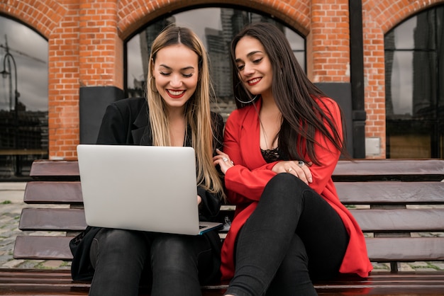 Portrait de deux jeunes amis à l'aide d'un ordinateur portable assis à l'extérieur. Concept d'amitié et de style de vie.