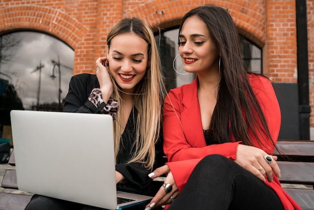 Portrait de deux jeunes amis à l'aide d'un ordinateur portable assis à l'extérieur