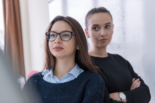 portrait de deux jeunes étudiantes debout devant un tableau blanc et regardant la caméra