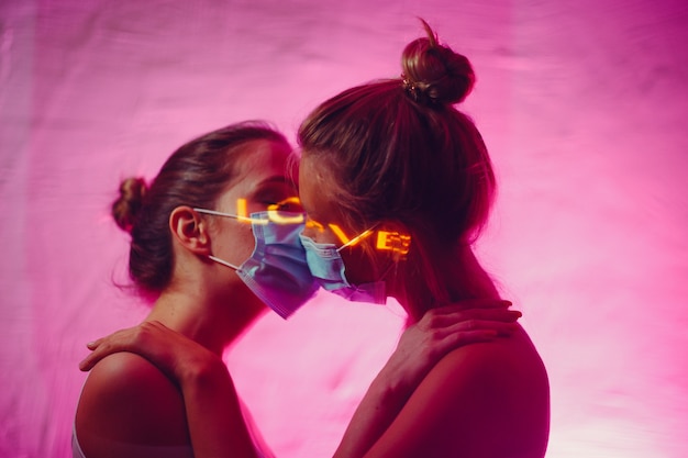 Portrait de deux jeunes femmes lgbt s'embrassant dans un masque médical