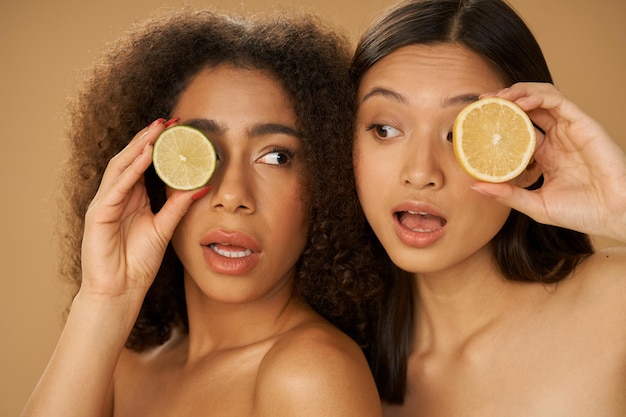 Portrait de deux jeunes femmes métisses drôles à la surprise de tenir le citron et le citron vert coupés