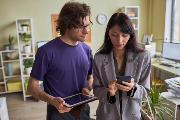 Portrait de deux jeunes hommes d'affaires utilisant une tablette et un smartphone au bureau pour partager des données.