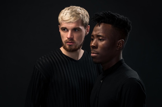 Portrait de deux jeunes hommes afro-américains et caucasiens debout sur fond noir tourné en studio