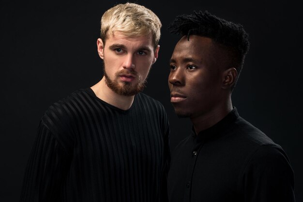 Portrait de deux jeunes hommes afro-américains et caucasiens debout sur fond noir tourné en studio