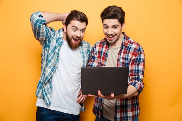 Portrait d'un deux jeunes hommes excités tenant un ordinateur portable