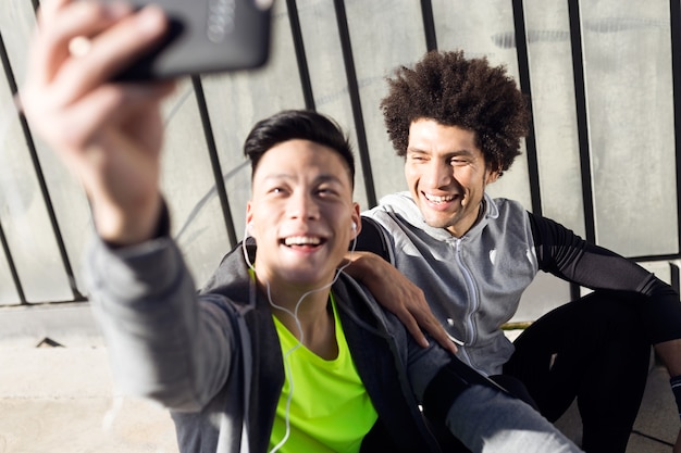 Portrait de deux jeunes hommes en forme et sportifs utilisant un téléphone portable dans la ville.