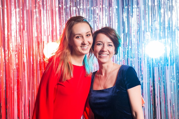 Portrait de deux jolies femmes heureuses en robes de soirée étreignant et regardant la caméra isolée sur fond brillant de couleur argentée. Fête d'anniversaire, vacances et concept de boîte de nuit.