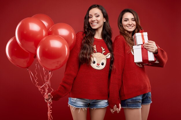 Portrait de deux jumeaux de meilleurs amis assez fous à la mode chandail d'hiver confortable avec des ballons de fête et des coffrets cadeaux posant