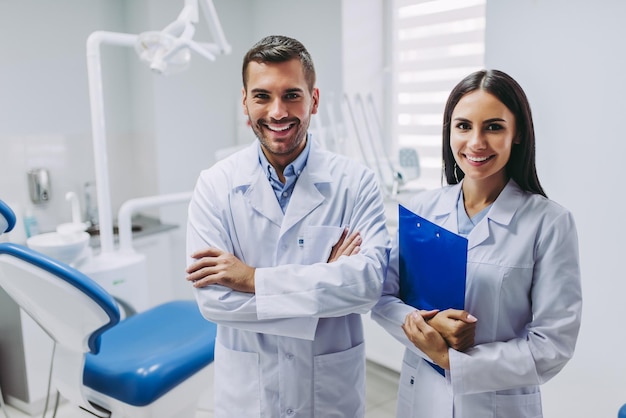 Portrait de deux médecins souriants regardant la caméra debout sur le lieu de travail dans une clinique dentaire moderne