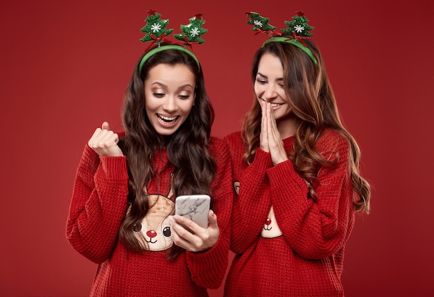 Portrait de deux meilleurs amis assez fous à la mode chandail d'hiver confortable hurlant de joie tout en regardant le téléphone