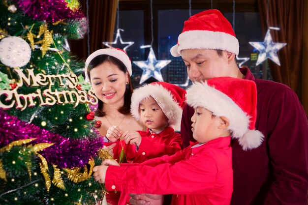 Portrait de deux petits enfants mignons et de leurs parents décorant un sapin de Noël à la maison