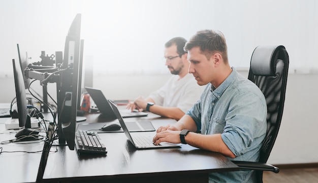 Portrait de deux programmeurs masculins professionnels travaillant sur l'ordinateur dans divers bureaux Technologies informatiques modernes développement de programmes d'intelligence artificielle applications et concept de jeux vidéo