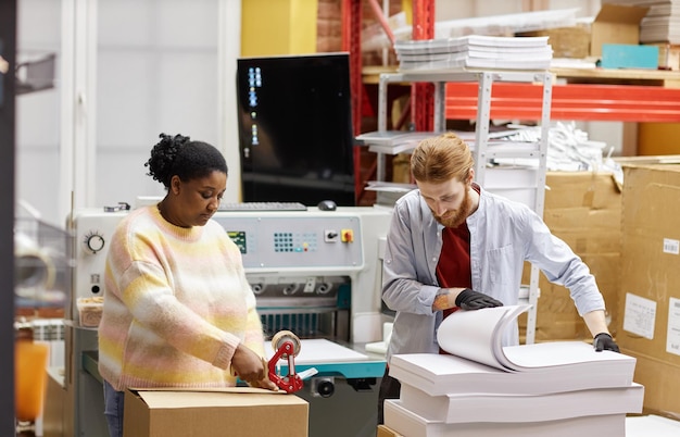 Portrait de deux travailleurs ouvrant des boîtes avec du papier dans l'espace de copie de l'imprimerie industrielle