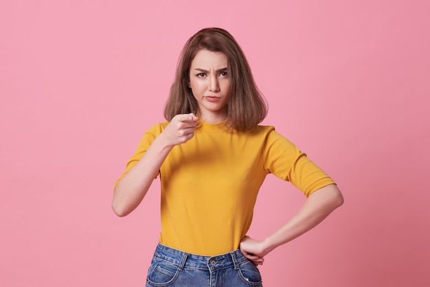 Portrait de doigt pointé en colère jeune femme à la caméra sur rose.