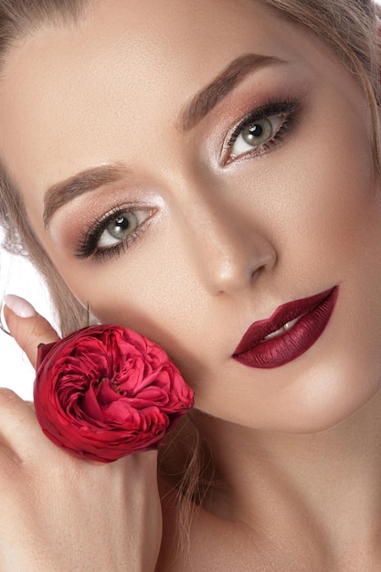 Portrait doux glamour d'une jeune fille avec une fleur rouge dans ses mains Beau maquillage et coiffure Photographié fond isolé blanc