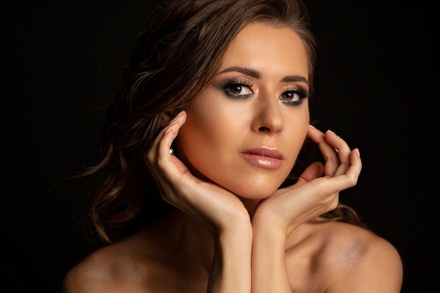 Portrait dramatique d'un modèle bronzé brune glamour avec un maquillage parfait et des épaules nues posant au studio
